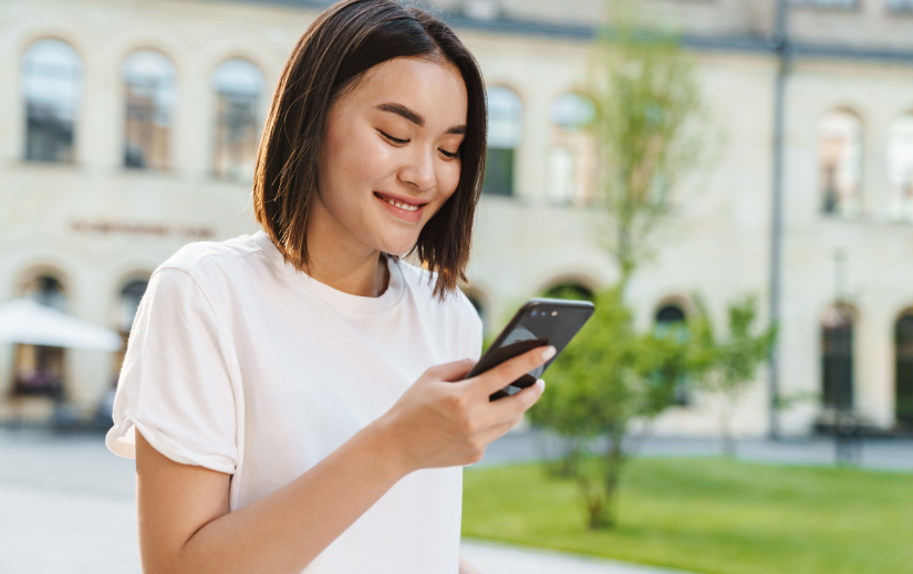 Smiling woman in white t-shirt looking at her phone, ideal for social media video ads or paid advertising visuals.